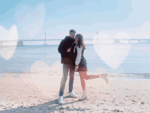 a man and a woman pose for a picture on a beach with a bridge in the background