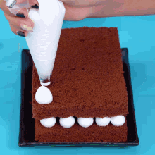 a person is frosting a chocolate cake on a blue background