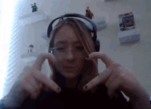 a woman wearing headphones and glasses is making a heart shape with her hands