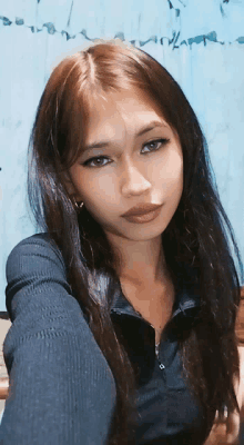 a woman with long brown hair is taking a selfie in front of a blue wall