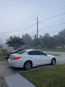 a white infiniti is parked in a foggy driveway next to other cars