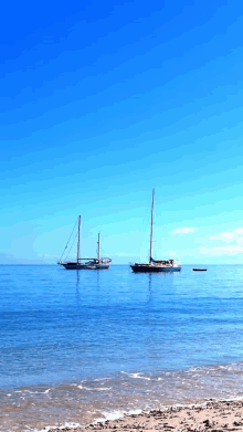 two sailboats are floating on the water near the beach