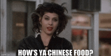 a woman in a black jacket is standing in front of a building and asking how 's ya chinese food .