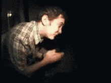 a man in a plaid shirt is standing in the dark looking at something