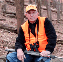 a man wearing an orange vest and an orange hat with the number 12 on it is holding a rifle