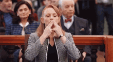 a woman is sitting in front of a microphone in a courtroom and covering her mouth with her hands .