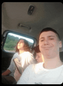 a man is taking a selfie in the back seat of a car while a woman looks out the window .