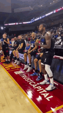 a group of basketball players are sitting on the sidelines in front of a sign that says " trust capital "