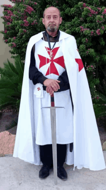 a man wearing a white cape with a red cross on it holds a sword