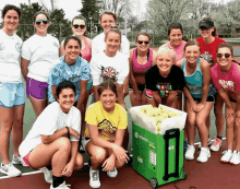 a group of young women are posing for a picture on a tennis court with a cooler full of tennis balls