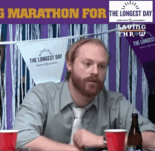 a man with a beard is sitting at a table in front of a banner that says marathon for the longest day