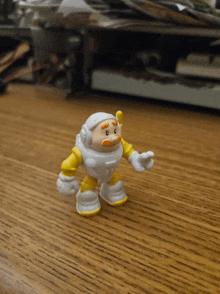 a toy with a white helmet and yellow pants is standing on a wooden surface