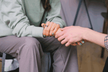 a woman in a green sweatshirt is holding another woman 's hand with blue nail polish