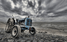 a blue ford tractor is parked on a cobblestone beach