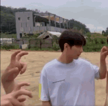 a young man in a white t-shirt is standing in a dirt field with his hands in the air .