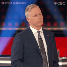 a man in a suit and tie stands in front of a blue background with the words family feud canada on it