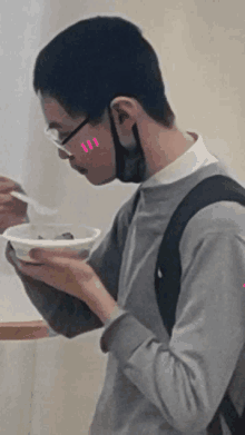 a young man wearing glasses and a mask is eating a bowl of food