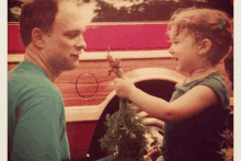 a little girl is holding a bunch of carrots next to her father