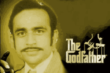 a man with a mustache and glasses is standing in front of a poster for the godfather