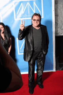 a man giving a peace sign on a red carpet in front of a banner that says music in media