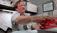 a man is using a stapler in an office cubicle with a framed certificate on the wall that says the office supply company