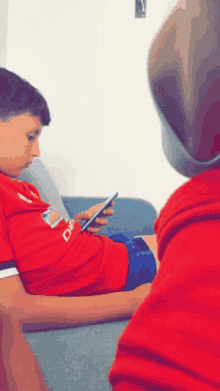 a boy in a red shirt with the word chevrolet on it looks at his phone