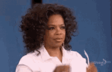 oprah winfrey is wearing a white shirt and holding a pen in her hand .