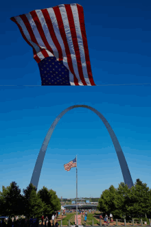 a large american flag is flying in front of a large arch