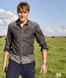 a man in a denim shirt and sweatpants stands in a field