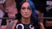 a woman with blue hair is standing in a wrestling ring looking at the camera .