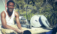 a man sits on the ground next to a lawn mower and trash cans