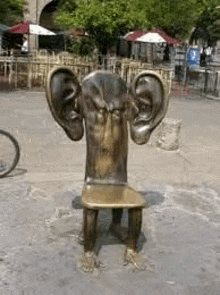 a statue of a person sitting on a chair with huge ears .