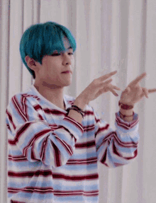 a young man with blue hair is wearing a striped shirt and making a peace sign