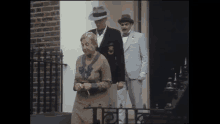 two men and a woman are standing outside of a building with a man wearing a hat that has the letter s on it