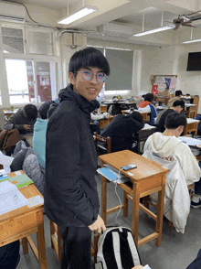 a boy in a black jacket stands in front of a classroom with a chair that says ' a ' on it