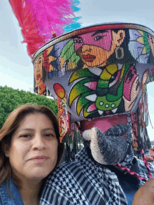 a woman stands next to a man wearing a colorful hat with a painting of a woman on it