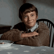 a young boy is sitting at a table with his arms crossed and a bowl of cereal in front of him