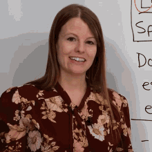 a woman in a floral shirt is smiling in front of a white board with the word do on it