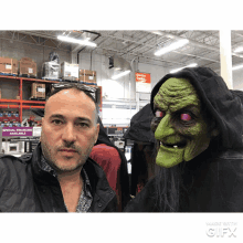 a man standing next to a green witch mask in front of a sign that says special savings available