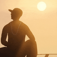 a silhouette of a man wearing a baseball cap and sunglasses looking at the sun