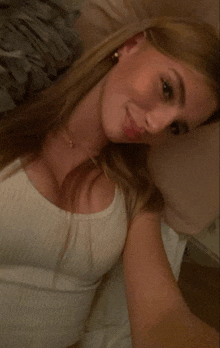 a woman in a white tank top is laying on a bed and taking a selfie