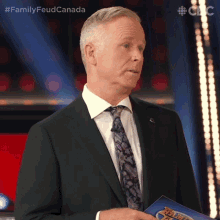 a man in a suit and tie is holding a clipboard with the words family feud canada written on it