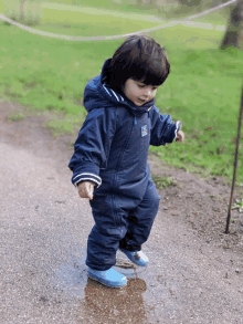 a little boy wearing a blue jacket with the letter e on it is standing in a puddle