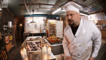 a man in a chef 's hat is standing in front of a table with candles and a picture of a man