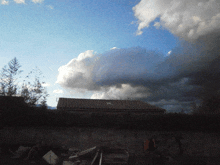 a cloudy sky over a house with a few trees in the foreground