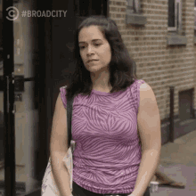 a woman in a zebra print shirt is standing in front of a brick building with #broadcity written on the bottom