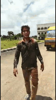 a man in a dirty shirt is walking down a street in front of a school bus that says shah