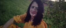 a woman in a yellow dress is sitting in the grass making a funny face .