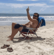 a shirtless man is sitting in a beach chair giving the middle finger