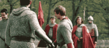 a man in chain mail is holding a sword in front of a group of men in armor